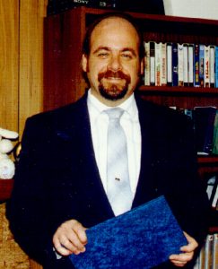 kevin-f-montague-in-suit-and-tie-holding-blue-folder